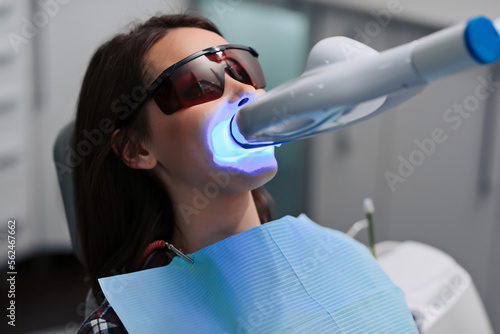 Close-up portrait of a female patient at dentist in the clinic. Teeth whitening procedure with ultraviolet light UV lamp.
