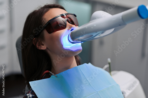 Close-up portrait of a female patient at dentist in the clinic. Teeth whitening procedure with ultraviolet light UV lamp. photo