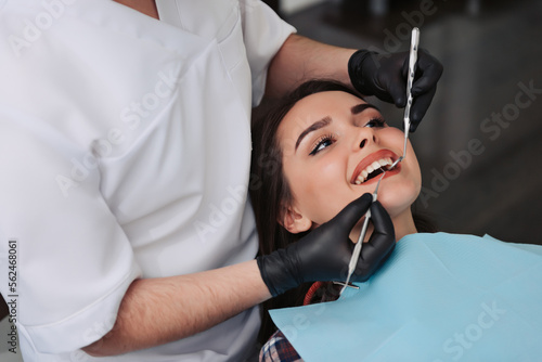 Dentist examining patient teeth with a mouth mirror and dental excavator. Close-up view on the woman s face