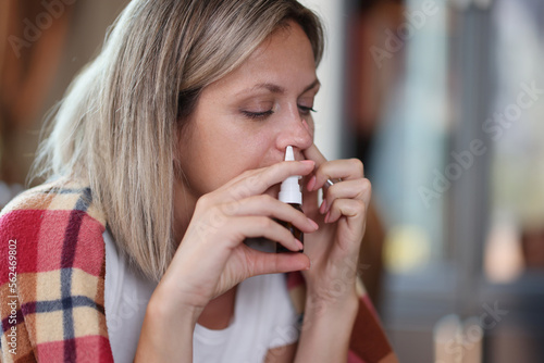 Sad woman with illness uses nasal spray while sitting at home close-up.
