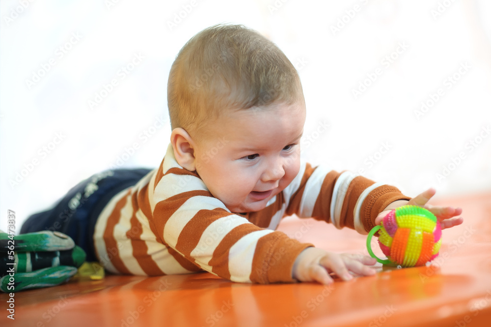 Baby plays with toys. Close-up view of cute baby boy lies on its stomach and play with toy. Playground for babies Baby plays with toys. Close-up view of cute baby boy lies on its stomach and play with toy. Playground for babies