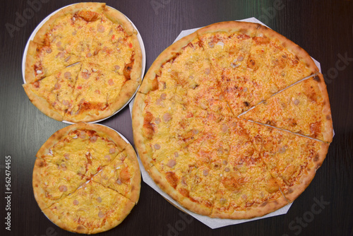 Three delicious fresh cheese pizzas with shrimp on black table, three different sizes for serving in pizzeria