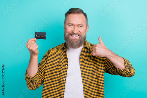 Photo of bank promoter man wear checkered shirt like recommend new black credit card shopaholic wireless pay isolated on aquamarine color background © deagreez
