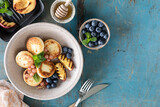 Cottage cheese pancakes, cheesecakes, ricotta fritters with fresh blueberries, currants and peaches on a plate. Healthy and delicious breakfast for the holiday. Blue wooden background