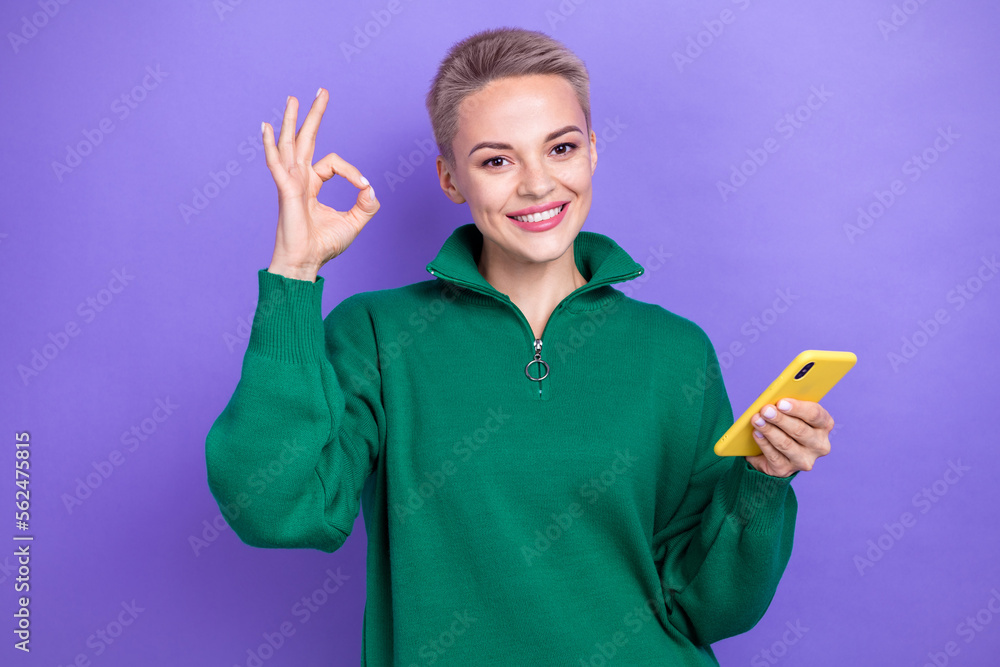 Photo of satisfied attractive freelancer blonde short hairdo woman hold phone show okey sign recommend this job isolated on purple color background Photo of satisfied attractive freelancer blonde short hairdo woman hold phone show okey sign recommend this job isolated on purple color background