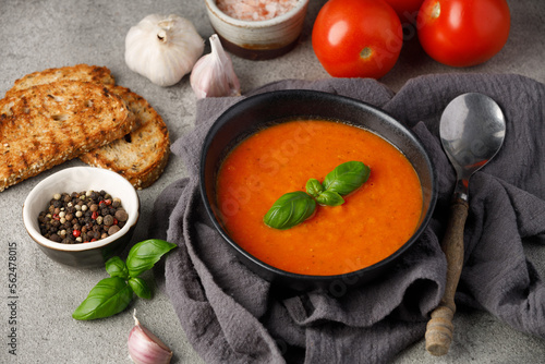 Classic tomato soup with basil and dried green herbs on a gray background