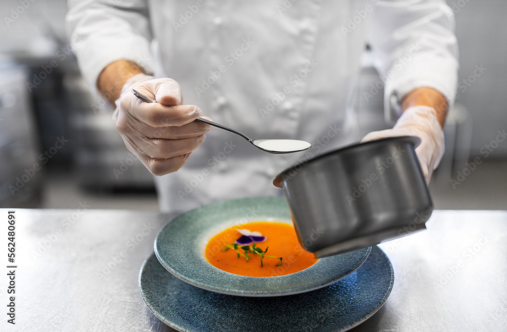 food cooking, profession and people concept - close up of chef serving plate of pumpkin cream soup and adding cream at restaurant kitchen