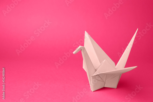 Origami art. Handmade paper crane on pink background, space for text photo
