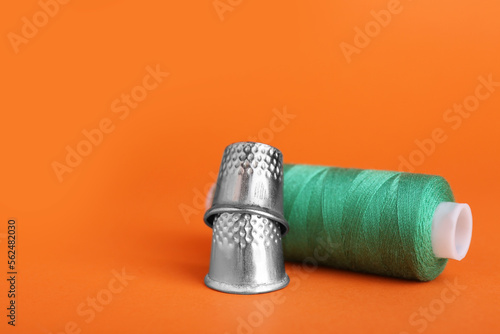 Thimbles and spool of green sewing thread on orange background  closeup. Space for text