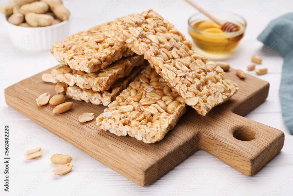 Board with tasty kozinaki bars, peanuts and honey on white wooden table Board with tasty kozinaki bars, peanuts and honey on white wooden table