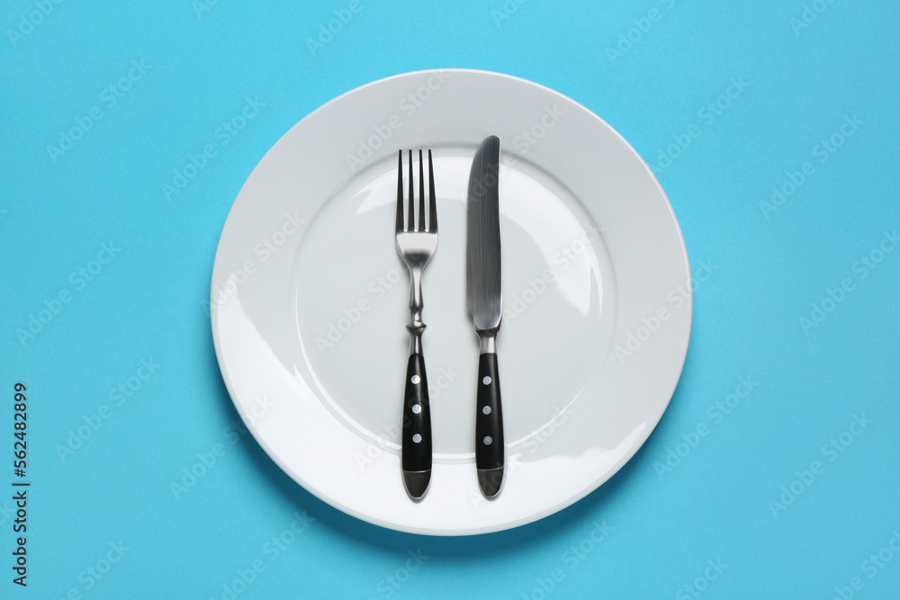 Clean plate with shiny silver cutlery on light blue background, top view Clean plate with shiny silver cutlery on light blue background, top view