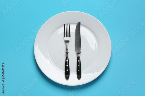 Clean plate with shiny silver cutlery on light blue background  top view