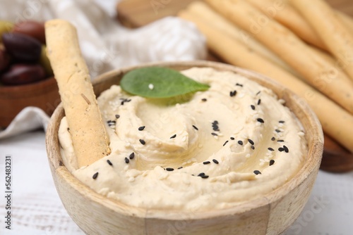 Delicious hummus with grissini stick on white wooden table, closeup