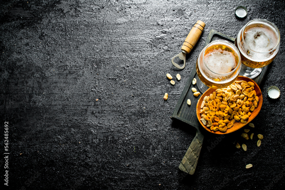 Two glasses of beer and peanuts in a bowl on a black cutting Board. Two glasses of beer and peanuts in a bowl on a black cutting Board.