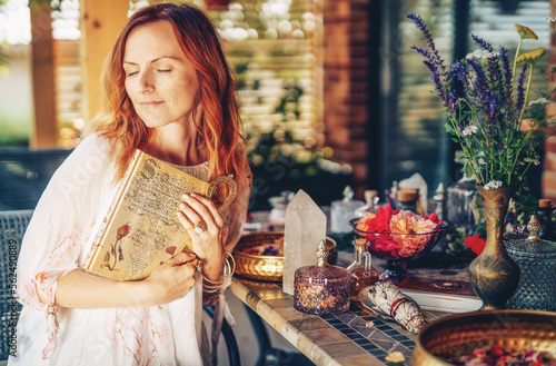 Woman holds ornamental book and Egyptian anch. Table with rose flower and essential oil. Spa and aromatherapy.
