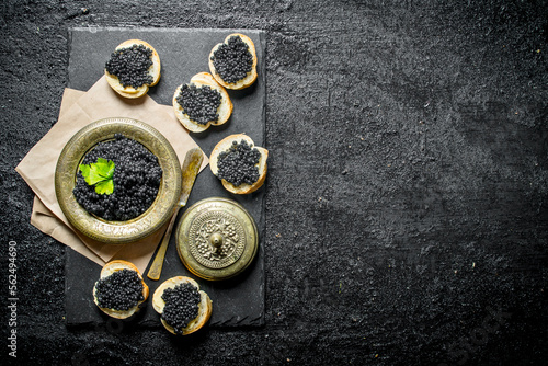 Sandwiches with black caviar and caviar in a bowl on paper with parsley.