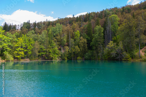 A lake of turquoise color among the hills covered with dense forest.