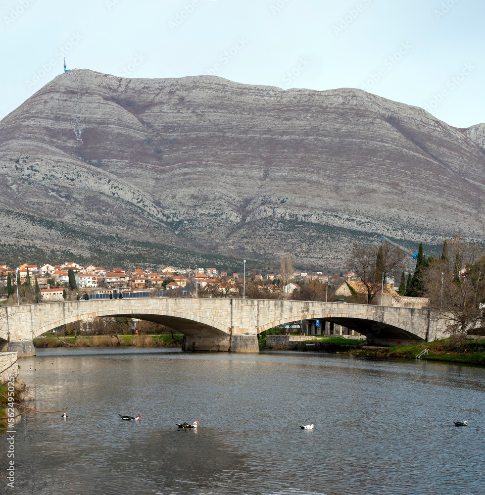 Trebinje town Stone bridge over river with ducks on water surface and hight rocky mountains at background