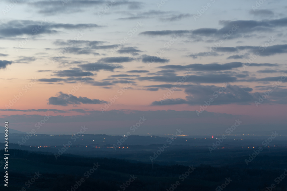 Light spots in dark countryside at twilight, hilly landscape and cloudy sky