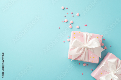 Saint Valentine's Day concept. Top view photo of light pink gift boxes with white ribbon bows and heart shaped sprinkles on isolated pastel blue background with copyspace