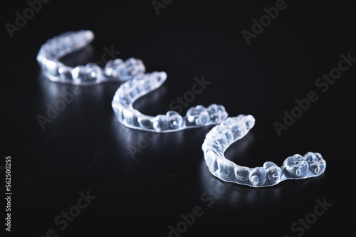 Three transparent aligners lie in a row on a black background. No people