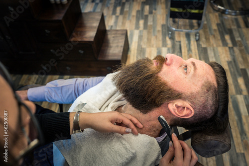 Hipster man at barbershop getting beard and hair cut - Female hairdresser woman hands using safety razor for trimming to classic gentleman cut - Barber shop concept