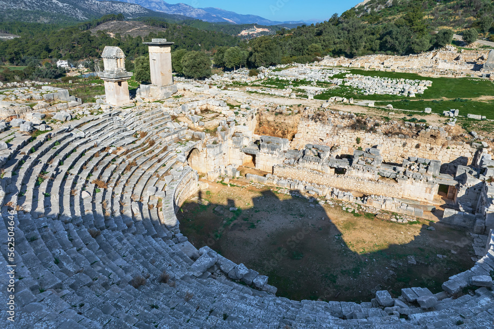 Naklejka premium Amazing view of theatre of Xanthos ancient city - part of Lycian way. Tomb monument of king Kybernis ( Harpy Tomb), Pillar Tomb on background. Popular travel destination in Antalya, Turkey