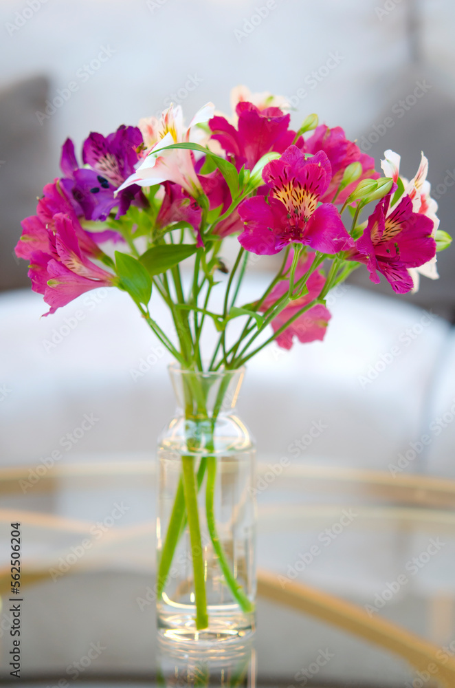 Beautiful bouquet in a vase on a glass table. Blooming pink, purple Alstroemeria. Home decor and decoration. Beautiful petals and green leaves in a floral arrangement.