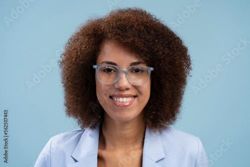 Close-up African American pretty woman, wearing eyeglasses, smiles looking at camera, isolated blue background
