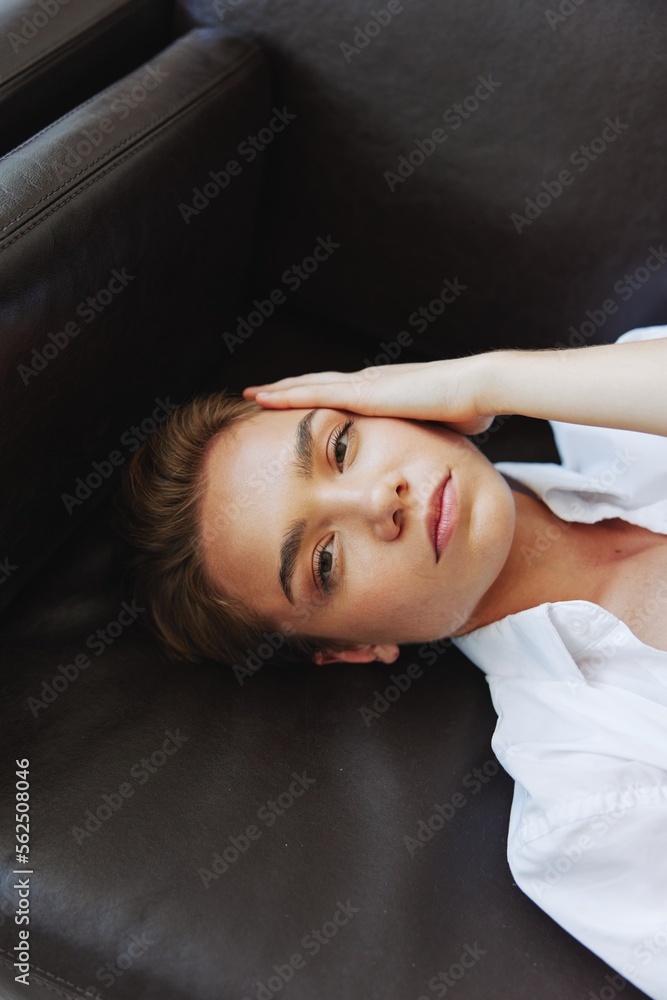 Women lying at home on the couch portrait with a short haircut in a white shirt, smile, depression in teenagers, home holiday Women lying at home on the couch portrait with a short haircut in a white shirt, smile, depression in teenagers, home holiday