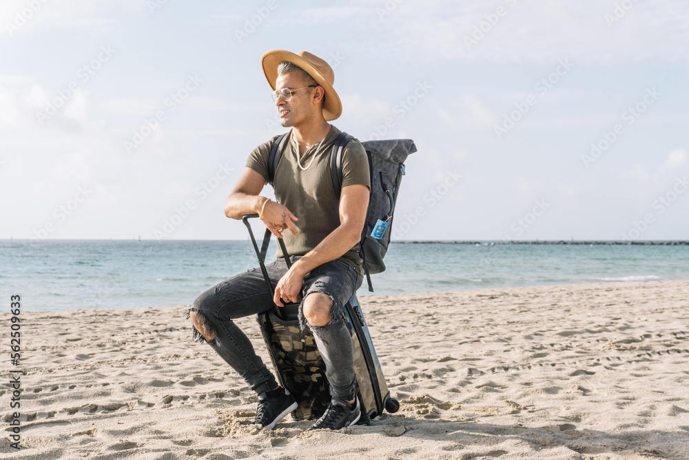 Close up of a lost man sitting on his small suitcase and looking at the sea on the beach,