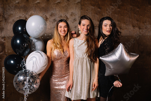 Beautiful young interracial girls with holiday make up smiling looking at camera indoors. Blonde and two brunettes wear dresses on holiday. Bachelorette party concept