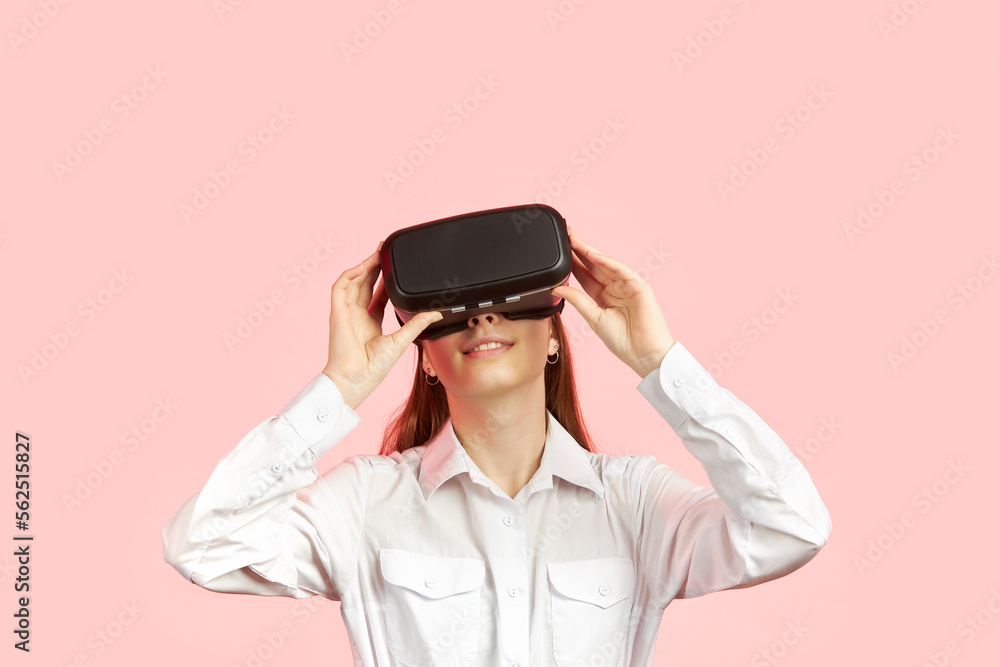 Young teen girl in a virtual reality helmet isolated on a pink background plays a 3d computer game. Young teen girl in a virtual reality helmet isolated on a pink background plays a 3d computer game.