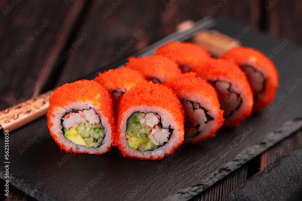 California sushi roll with crab, avocado, cucumber and tobiko caviar served on black board close-up - Japanese food California sushi roll with crab, avocado, cucumber and tobiko caviar served on black board close-up - Japanese food