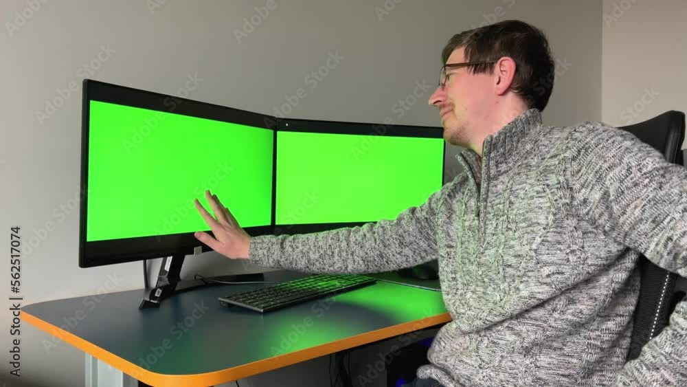 young programmer artist web designer looks at monitor with two green screens chromakey he gently swallows with hand on one of monitors advertisement can be he is very happy after that he laughs hard young programmer artist web designer looks at monitor with two green screens chromakey he gently swallows with hand on one of monitors advertisement can be he is very happy after that he laughs hard