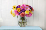 a lush bouquet of chrysanthemums, asters and other autumn flowers in a glass vase on the table.