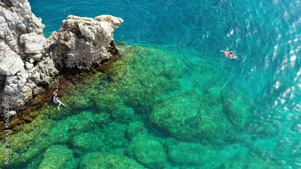 Aerial view of a young couple snorkeling above coral reef reaching deeper parts of the crystal clear water, Rhodes, Greece. Aerial drone view of a couple snorkeling swimming in crystal clear water. Aerial view of a young couple snorkeling above coral reef reaching deeper parts of the crystal clear water, Rhodes, Greece. Aerial drone view of a couple snorkeling swimming in crystal clear water.