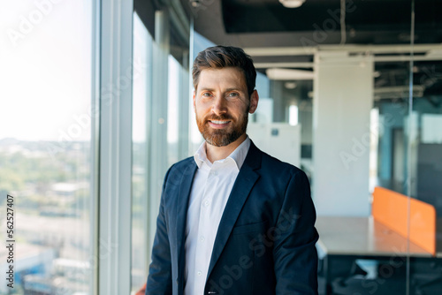 Successful person. Handsome businessman in formal wear standing in office near window, looking and smiling at camera photo
