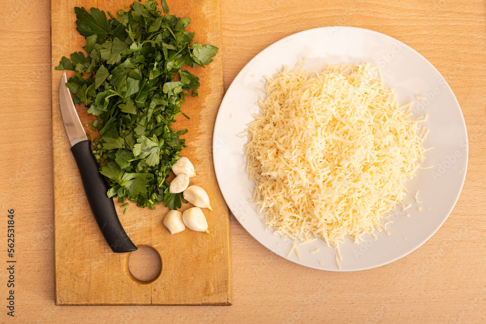 Ingredients for cooking. Chopped greens and garlic on the board. Grated cheese in a bowl.
