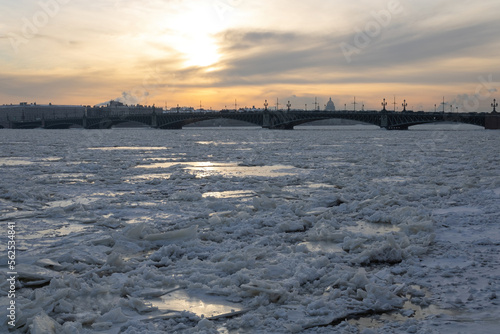 Ice floes on the frozen Neva river  bridge  sunset sky. Building silhouettes. St. Petersburg  early winter.