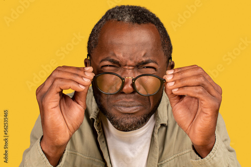 Concentrated african american middle aged man squinting eyes, takes off glasses, looks at camera