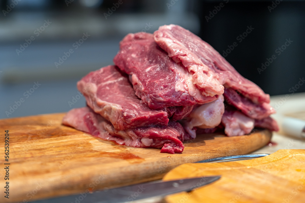 Heap of pieces raw beef steakes. Raw beef sliced meat on wooden cutting board on marbled countertop.