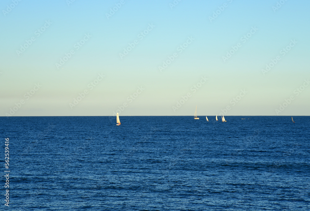Sailboat at sea on sailing on the waves. Yachtsman during training on a sailboat. Skiff and Sailboat in sea port near the Spanish coast. Sail sport in Yacht club. Sail boat on waves on sunset in sea.