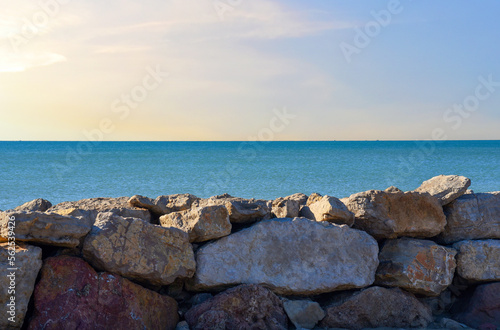 Breakwater, Stone wall at sea. Sea with waves against sunset. Stone pier at sea. Wave breaker at shoreline with stones. Waves in storm breaks on stones at pier. Masonry breakwater in ocean. stone