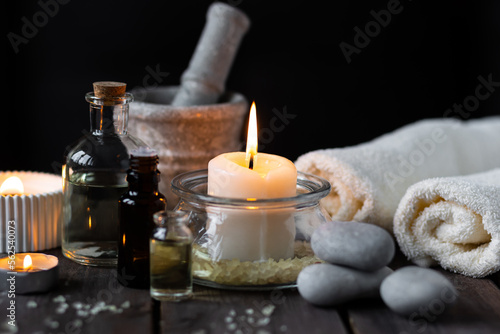 Spa setting with essential oil, candle, sea salt, pebbles, towel on dark wooden background. Massage, aromatherapy. Natural organic ingredients for relaxation, detention. Wellness in salon concept
