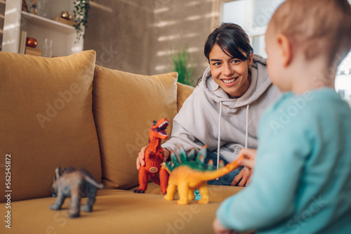Mother and toddler son playing with dinosaurs toys at home on the couch photo