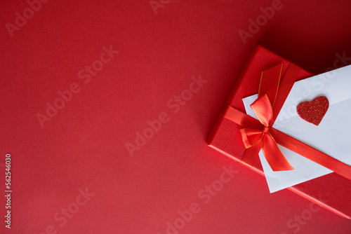 Romantic love letter in white envelope with Valentines heart and gift box with red ribbon on red background. Flat lay, top view, copy space. Happy Valentine's Day concept