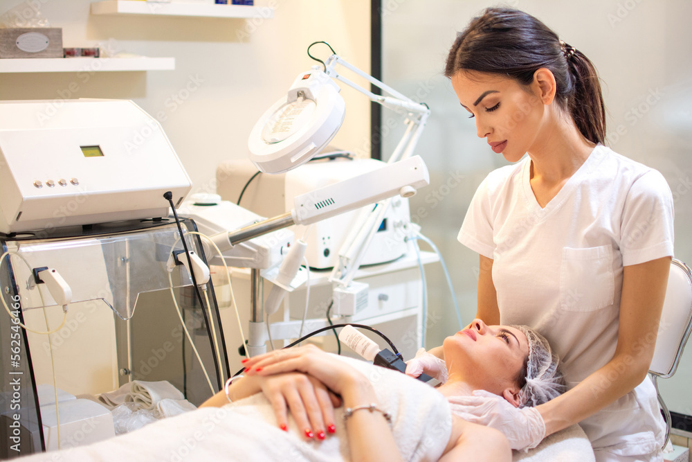 Doctor with Ultrasonic scraber doing procedure of ultrasonic cleaning of female client neck at beauty salon. Doctor with Ultrasonic scraber doing procedure of ultrasonic cleaning of female client neck at beauty salon.
