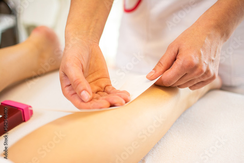 Close-up of a beautician waxing leg of woman with wax strip at a beauty spa.