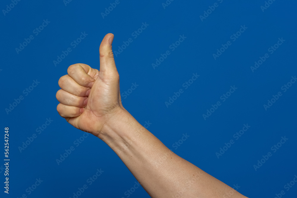 Thumb up hand sign. man's hand showing thumb up, like, ok, approval, accept, okay, good, positive hand gesture. Isolated on blue studio background.